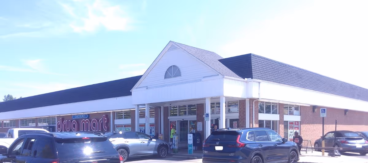 Exterior view of a Discount Drug Mart storefront with several parked cars.