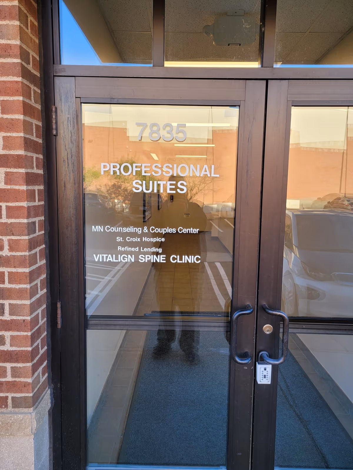 Double glass doors labeled Professional Suites with reflections outside and a brick wall.