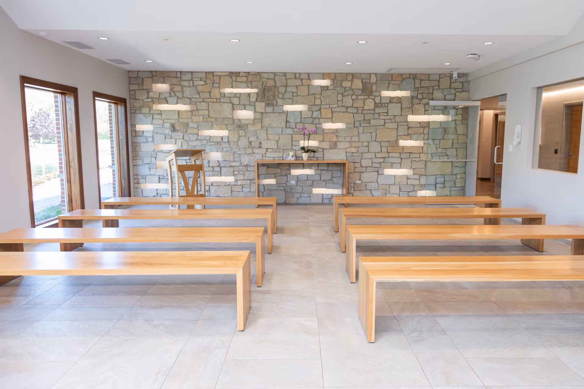 Bright waiting area with wooden benches, stone accent wall, and a small table with flowers.