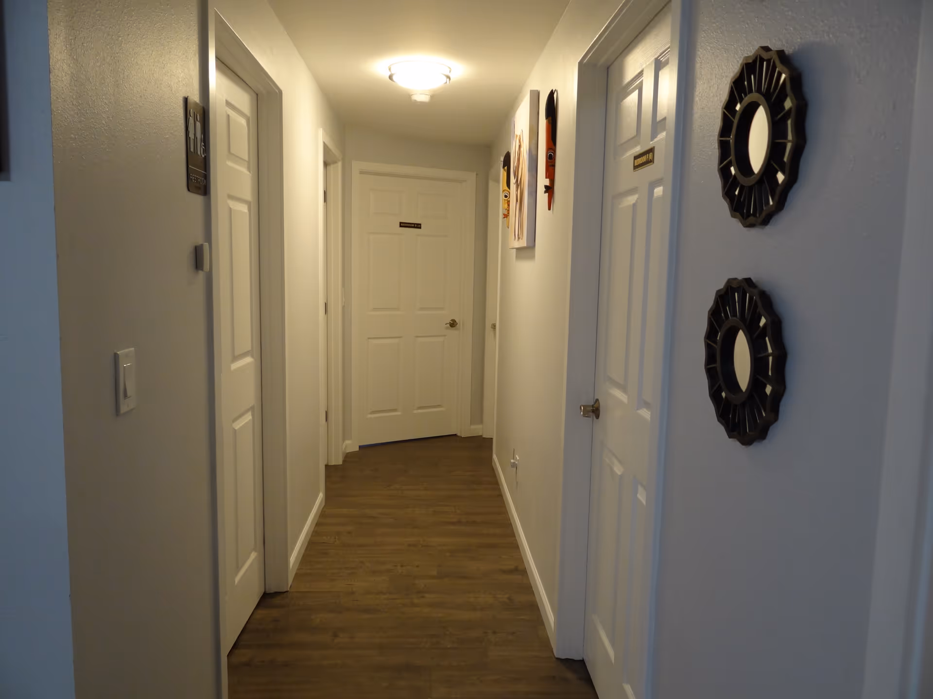 Narrow hallway with white doors, wood floor, and round wall mirrors.