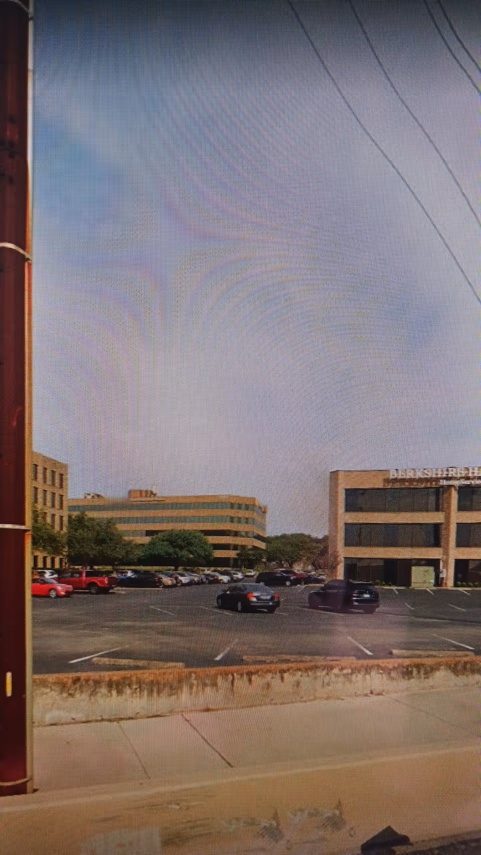 Exterior view of a parking lot and office-style buildings, sidewalk in foreground.