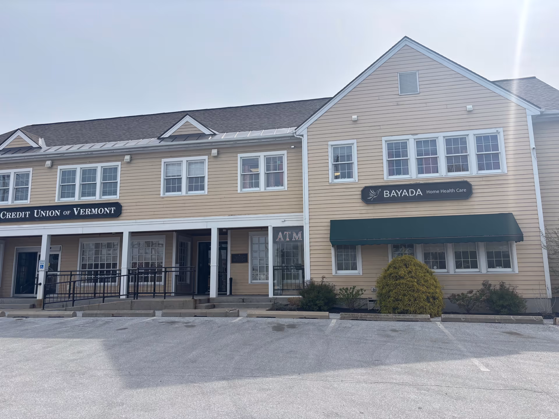 Two-story beige building with BayADA and Credit Union storefronts, parking lot in foreground.