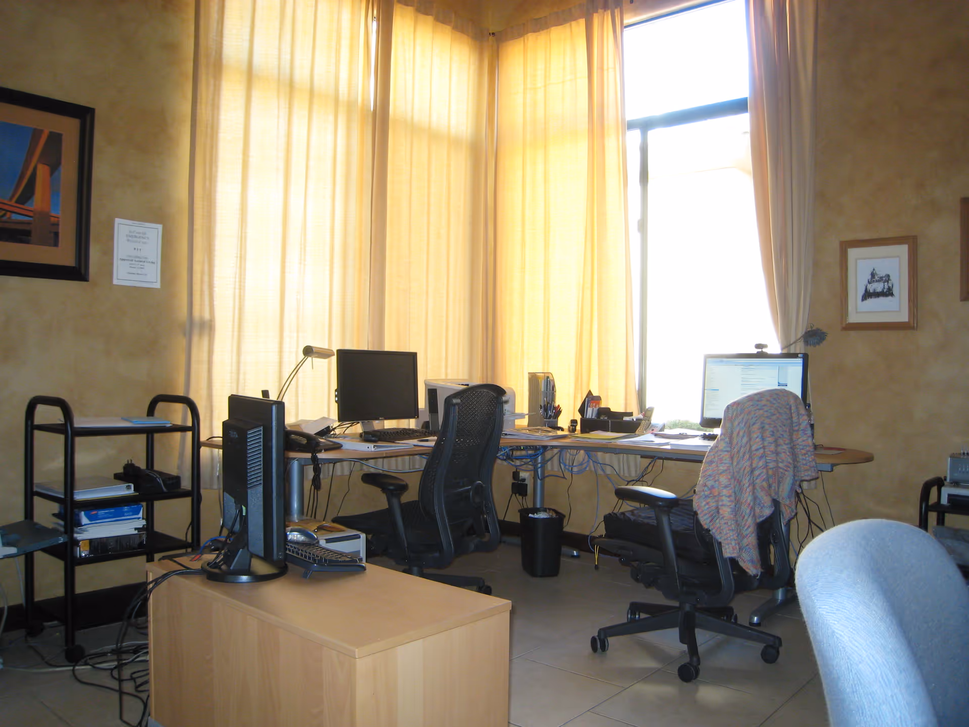 Open office area with desks, computers, chairs, and yellow-curtained windows