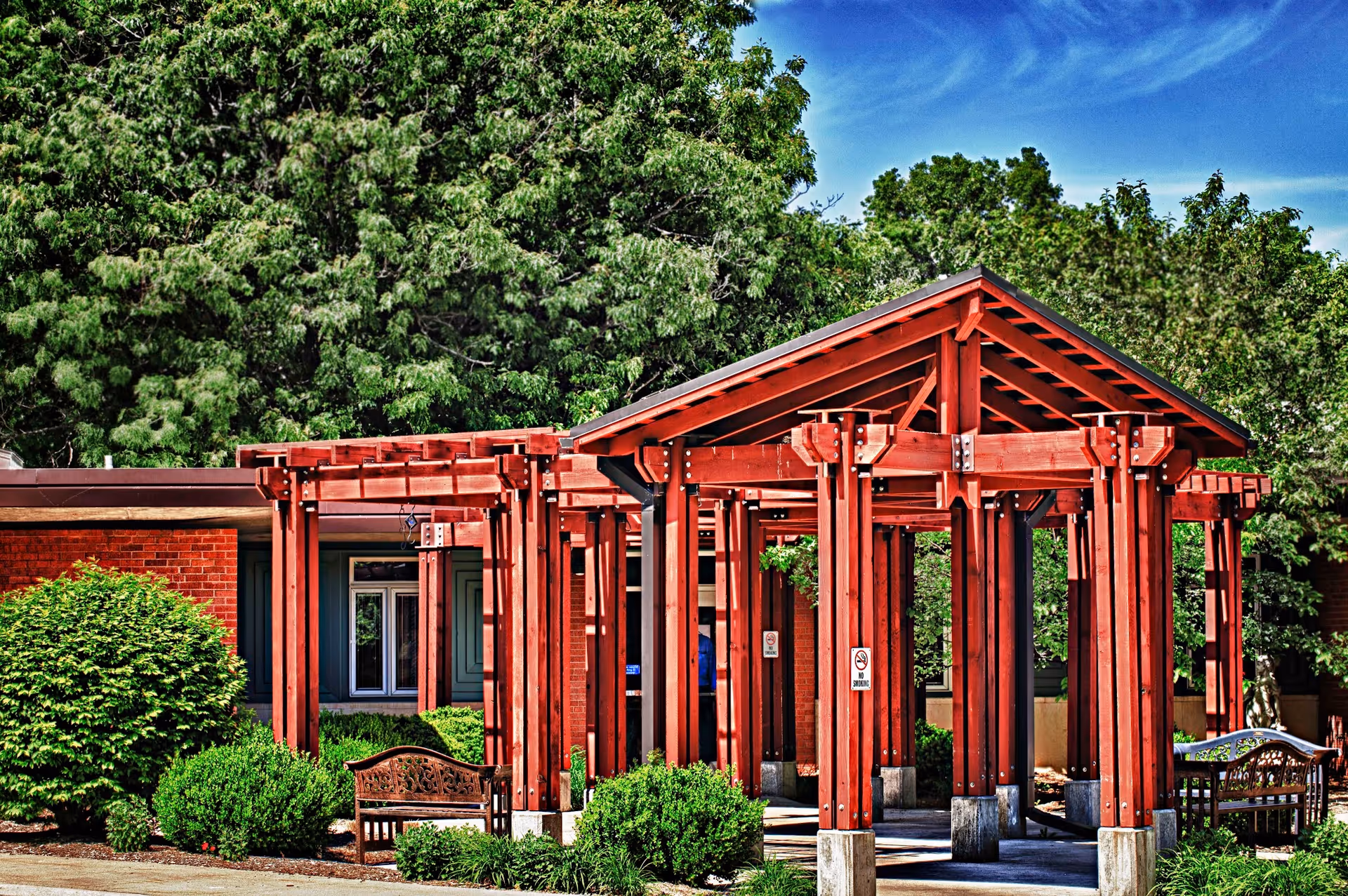 Red wooden pergola walkway outside Midland Care Connection with benches and greenery