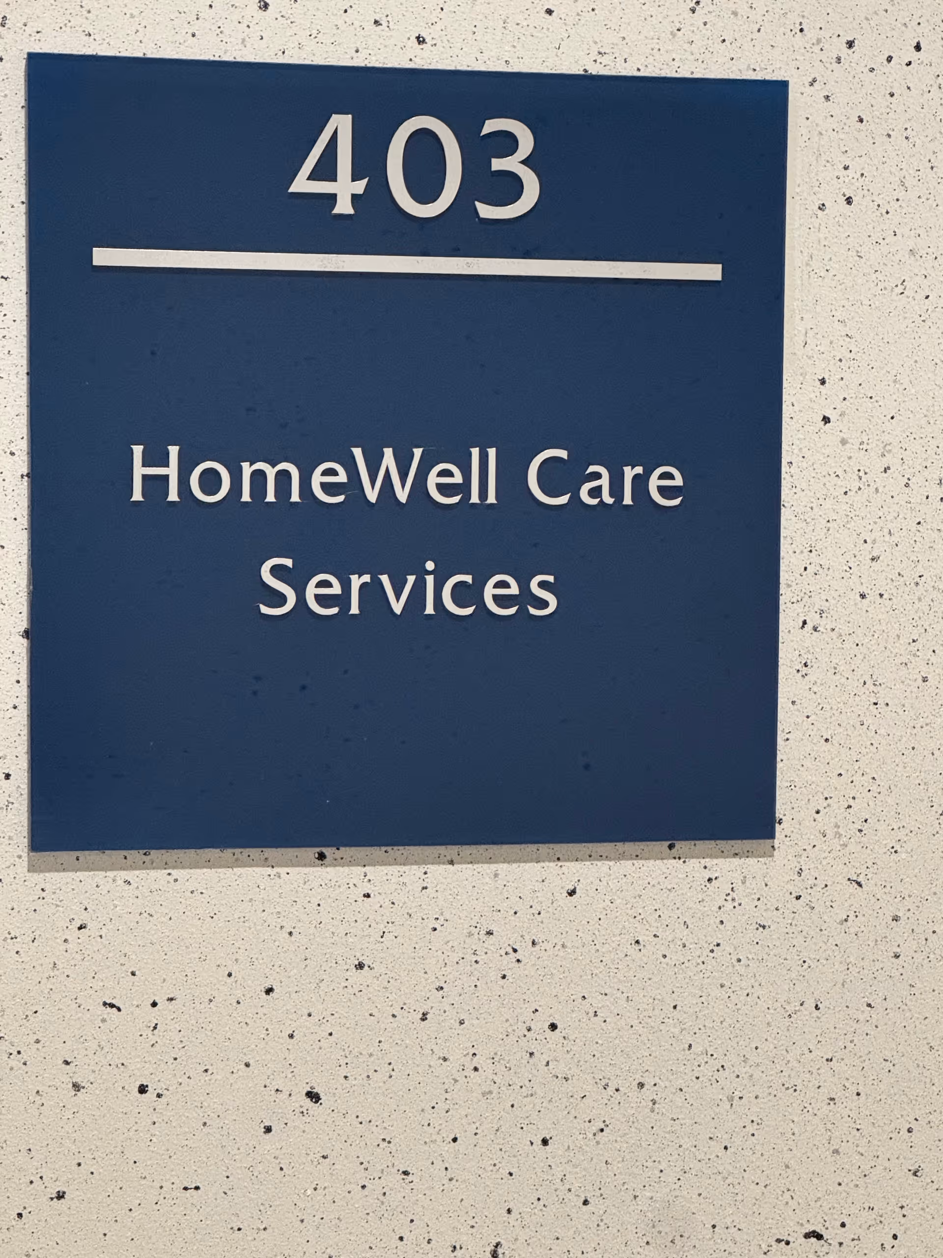 Blue sign on a speckled wall displays 403 and HomeWell Care Services.