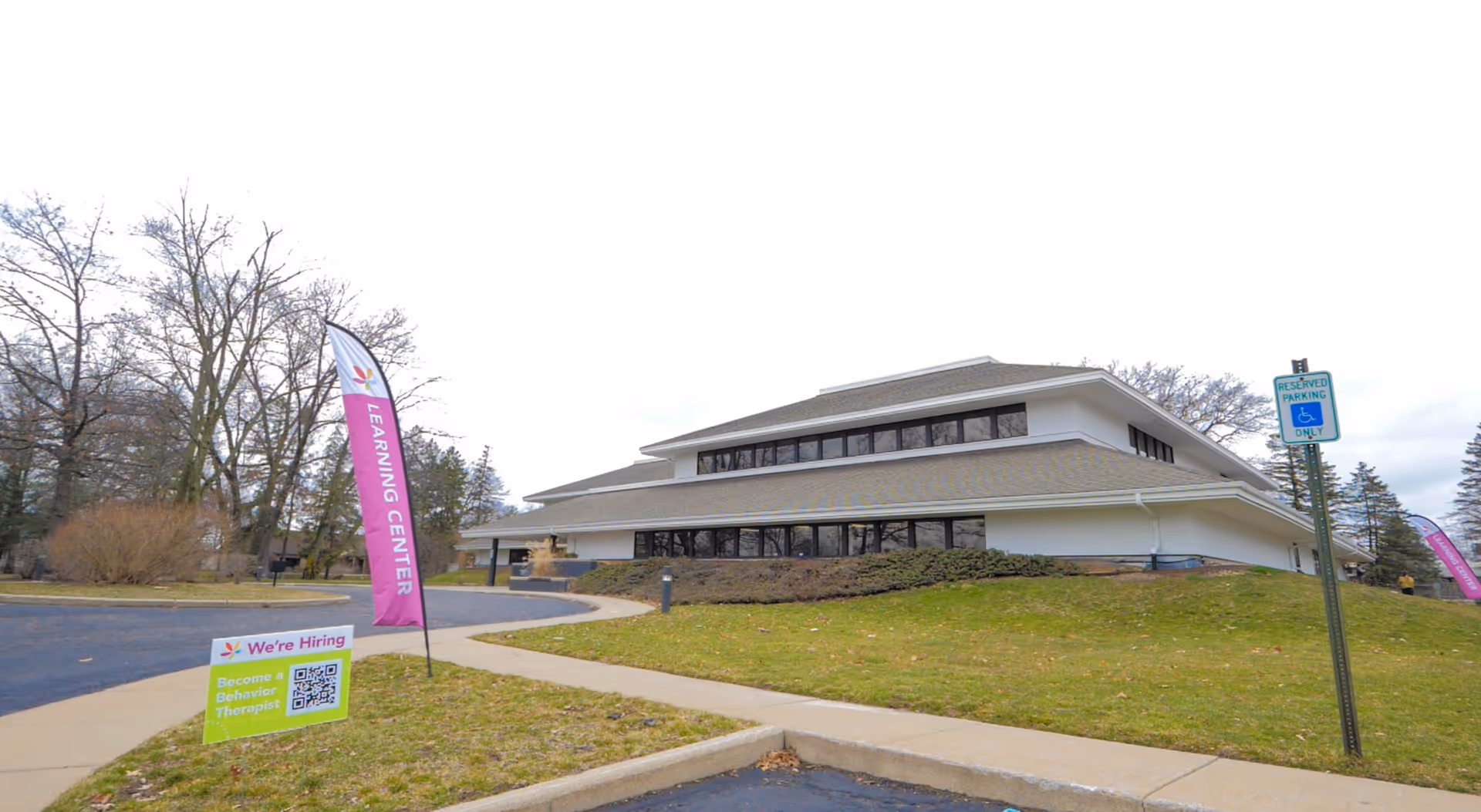 modern low-rise building with sloped roof, lawn, walkway, and purple flags outdoors