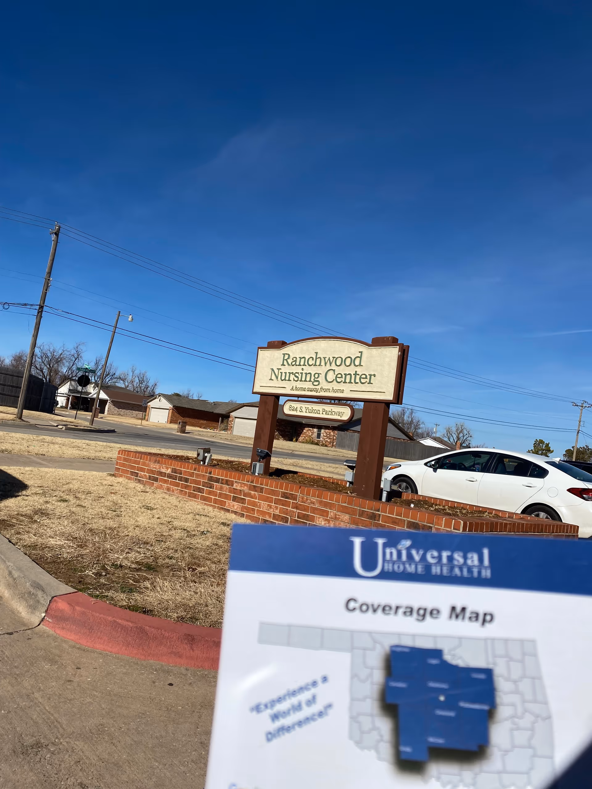 Outdoor view showing Ranchwood Nursing Center sign, brick planter, and Universal Home Health map pamphlet.
