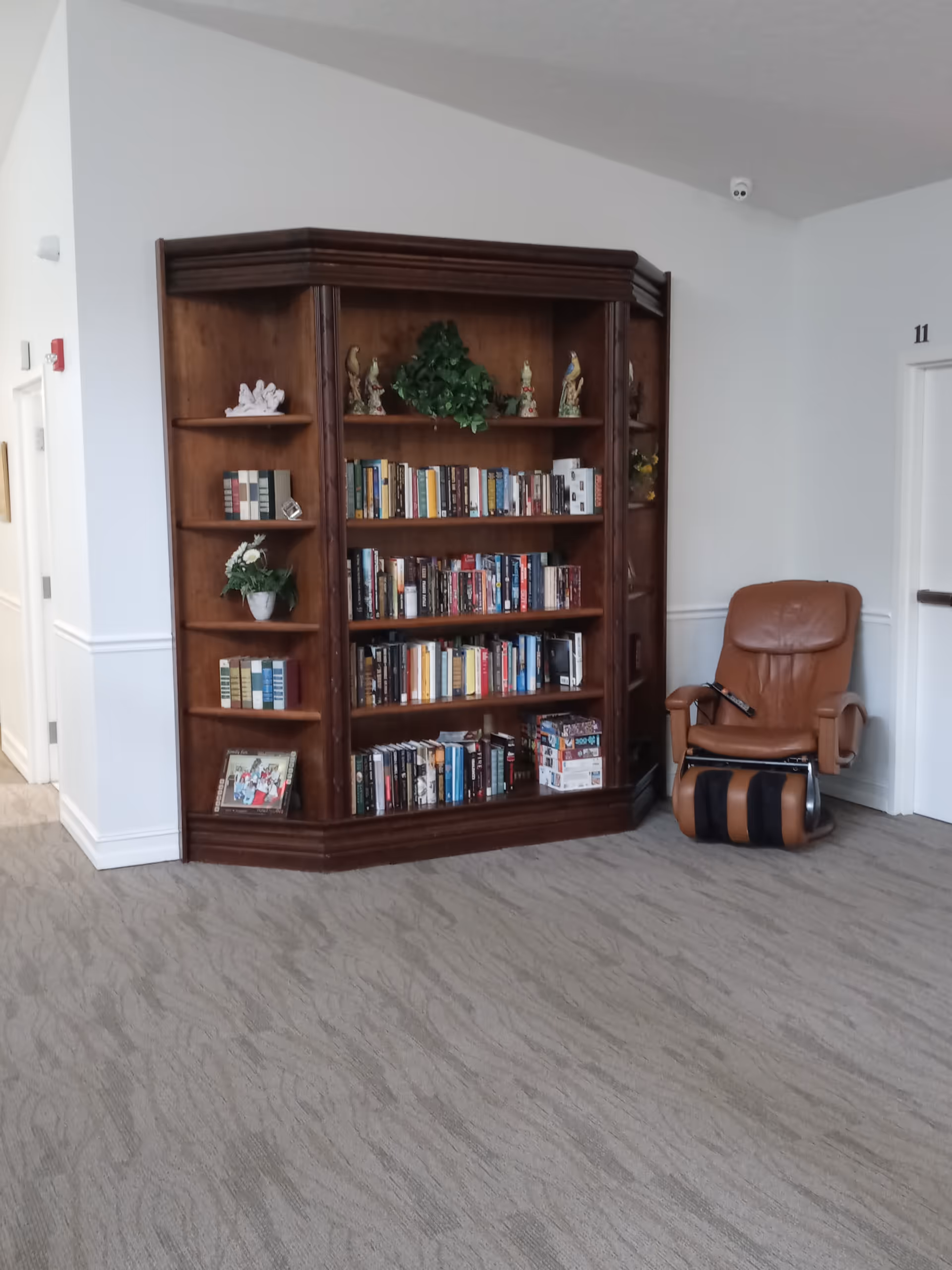 Wooden bookshelf filled with books beside a brown recliner chair in a quiet lounge.