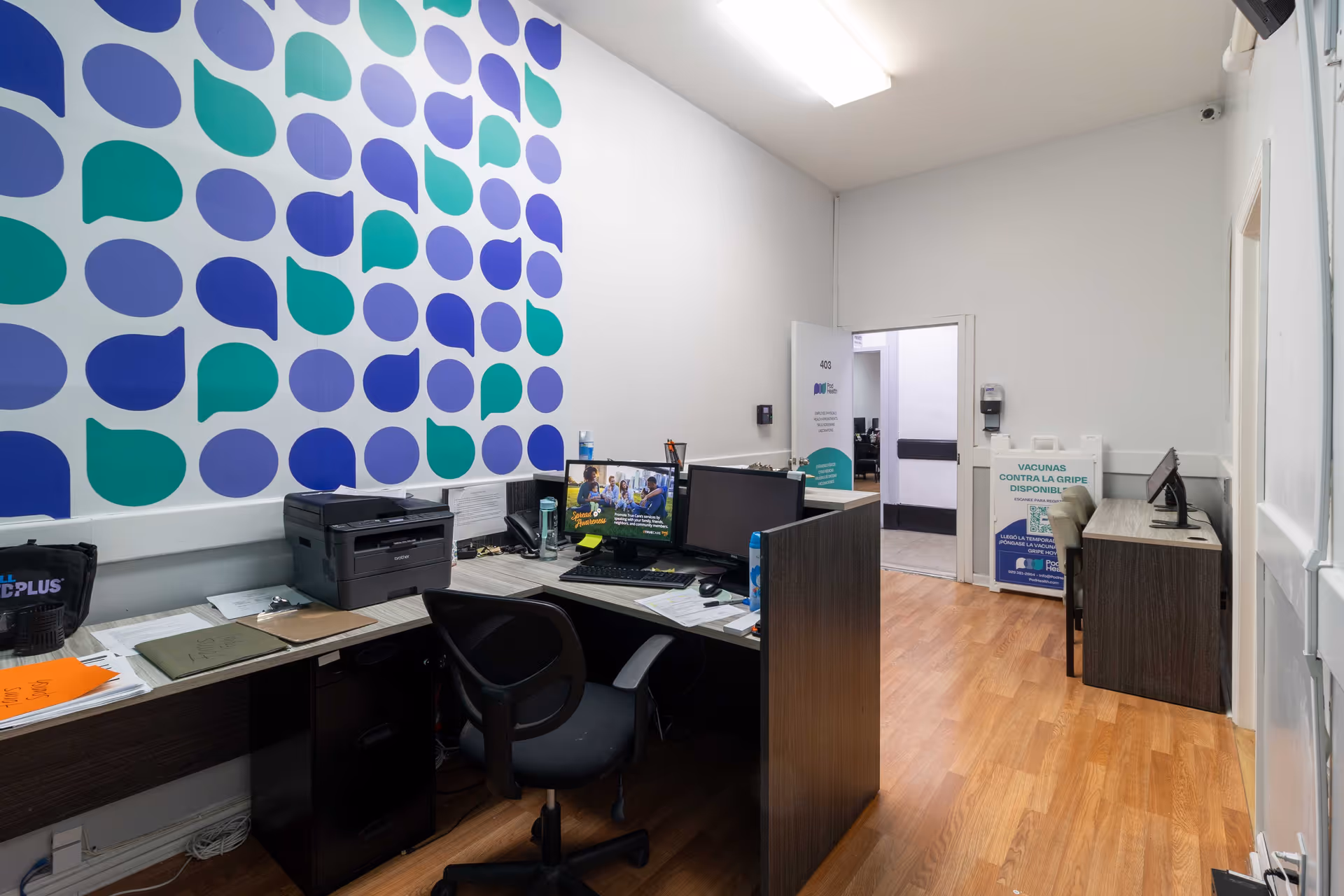 Office reception area with computer desk, printer, and colorful wall art in Pod Health facility.