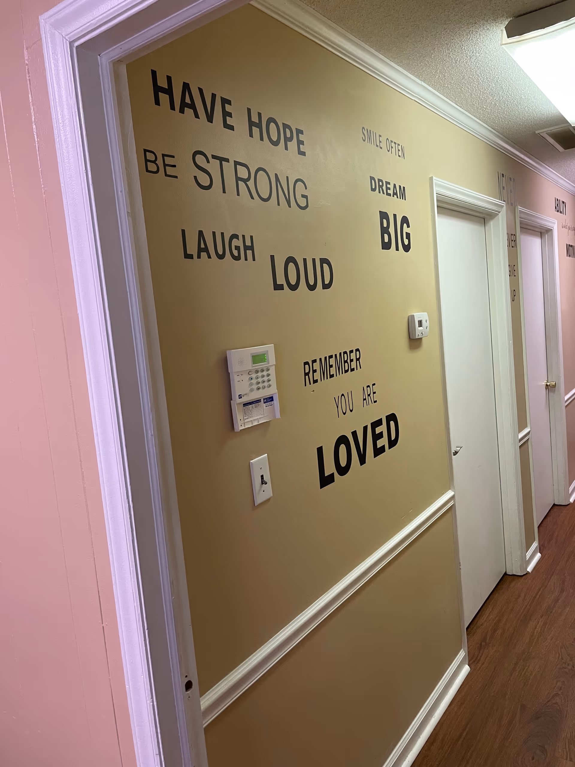 Interior hallway with tan wall art displaying inspirational quotes and a mounted thermostat.