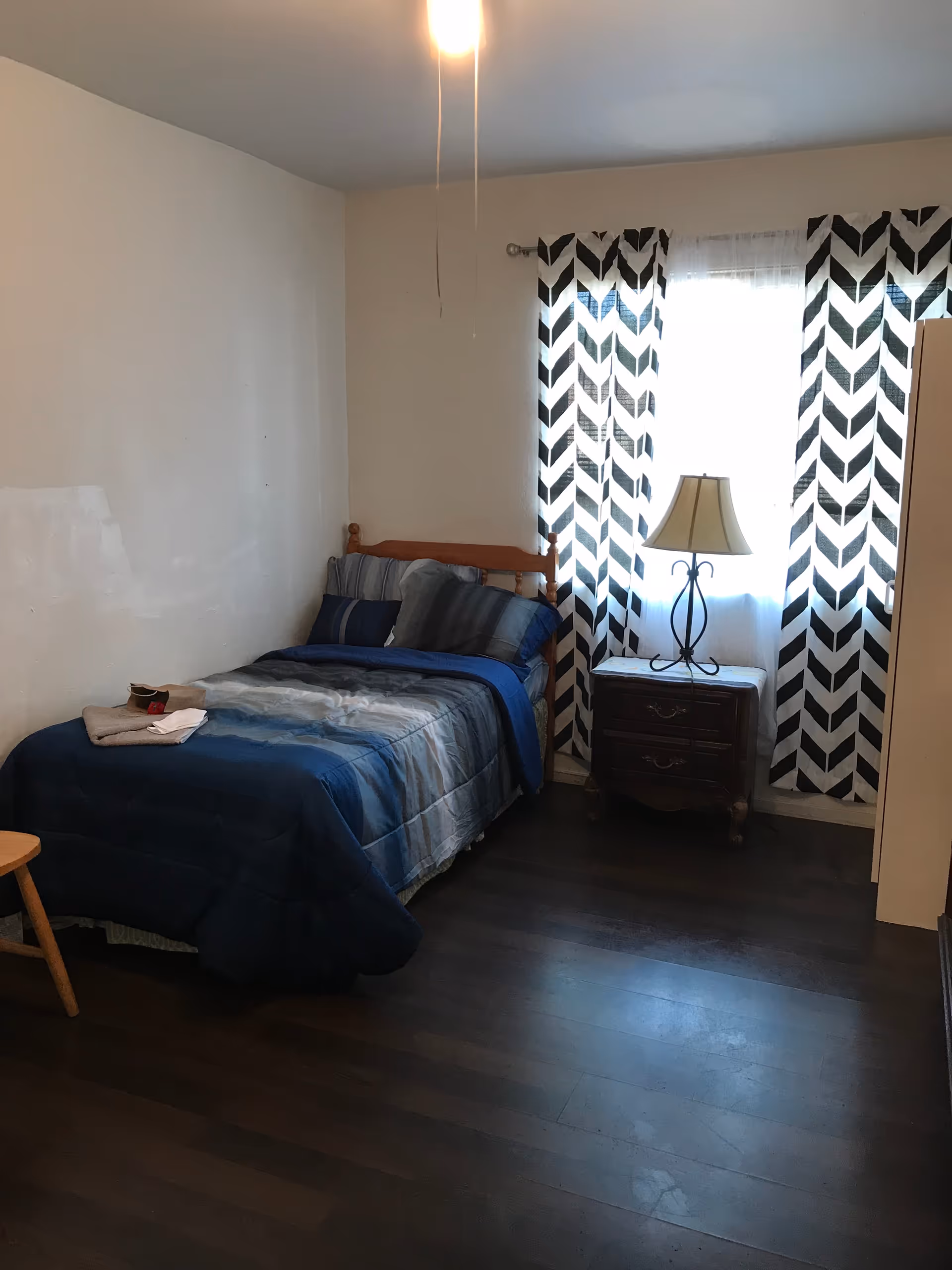 A single bed with blue bedding beside a nightstand and lamp.