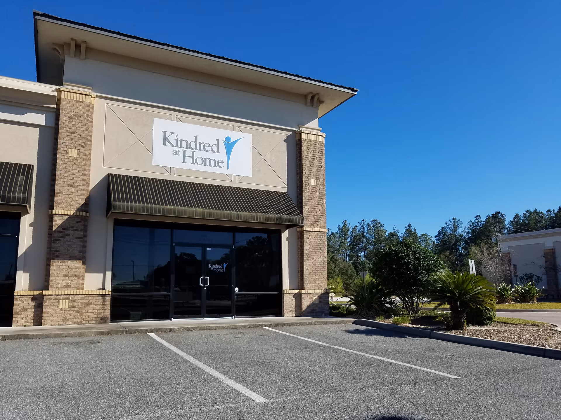 Exterior view of a building with a large Kindred at Home sign and glass entry doors.