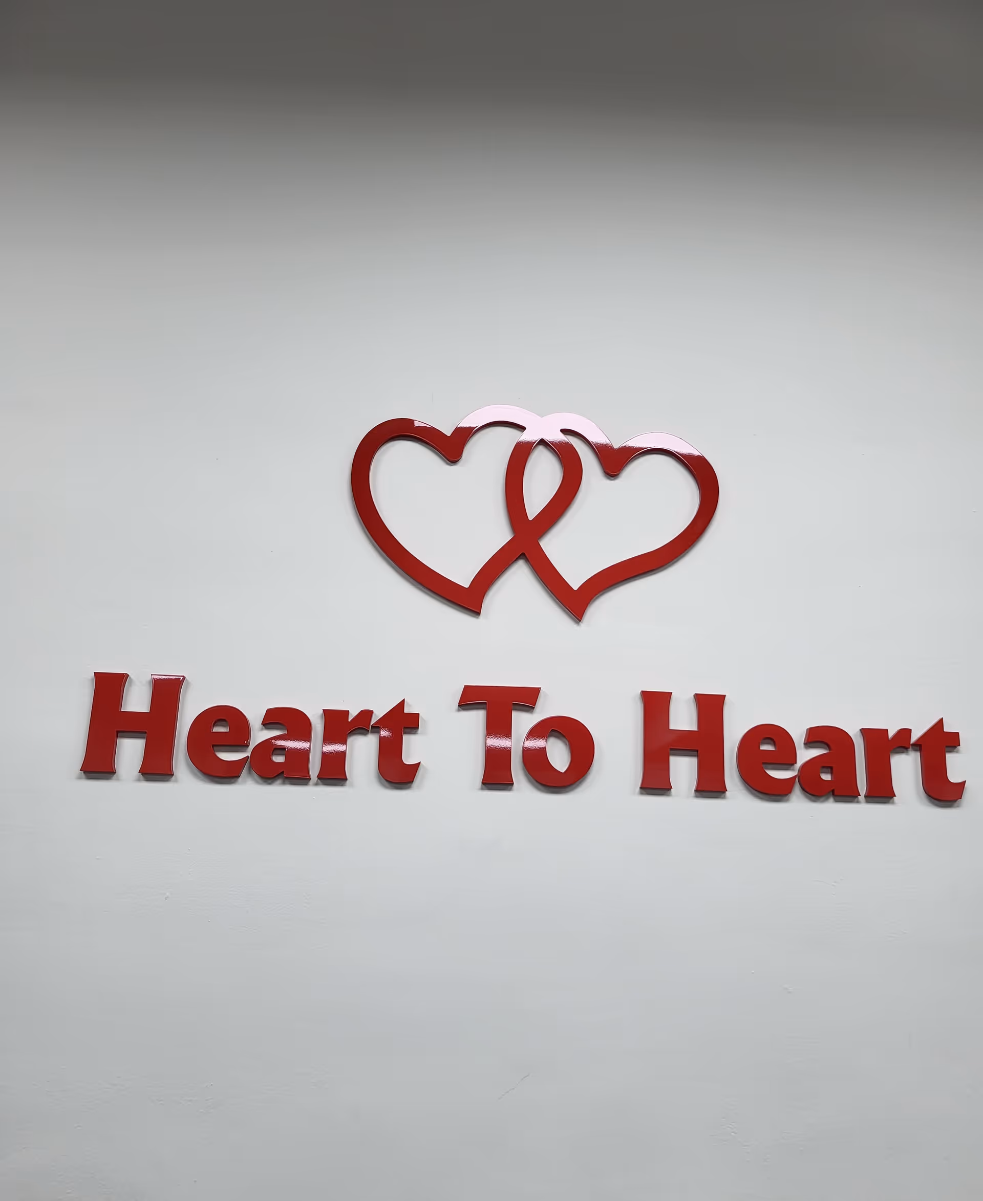 Red sign on a white wall reads Heart To Heart with two intertwined hearts.
