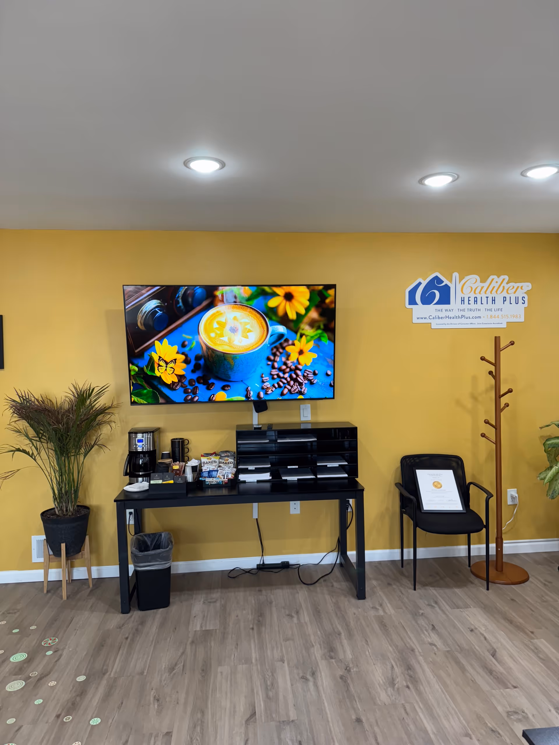 Interior lounge area with a yellow wall, television, coffee station, and seating.