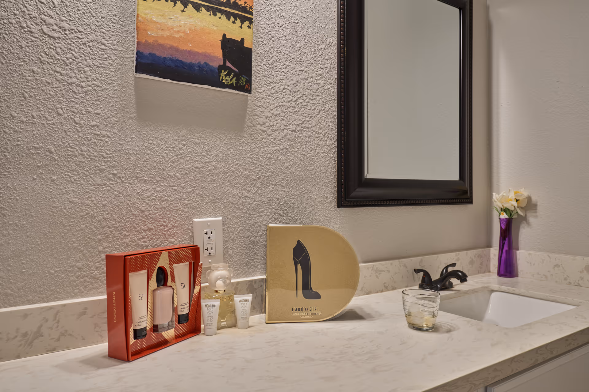 Bathroom sink countertop with toiletries, mirror, vase of flowers, and a high-heel sign.