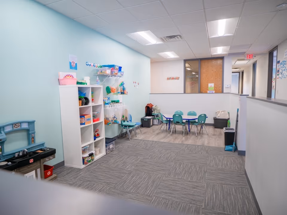 Indoor playroom with toy shelves, play kitchen, and small teal chairs.