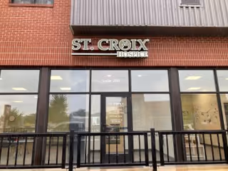 Brick storefront with large glass windows and a St. Croix Hospice sign above the entrance.