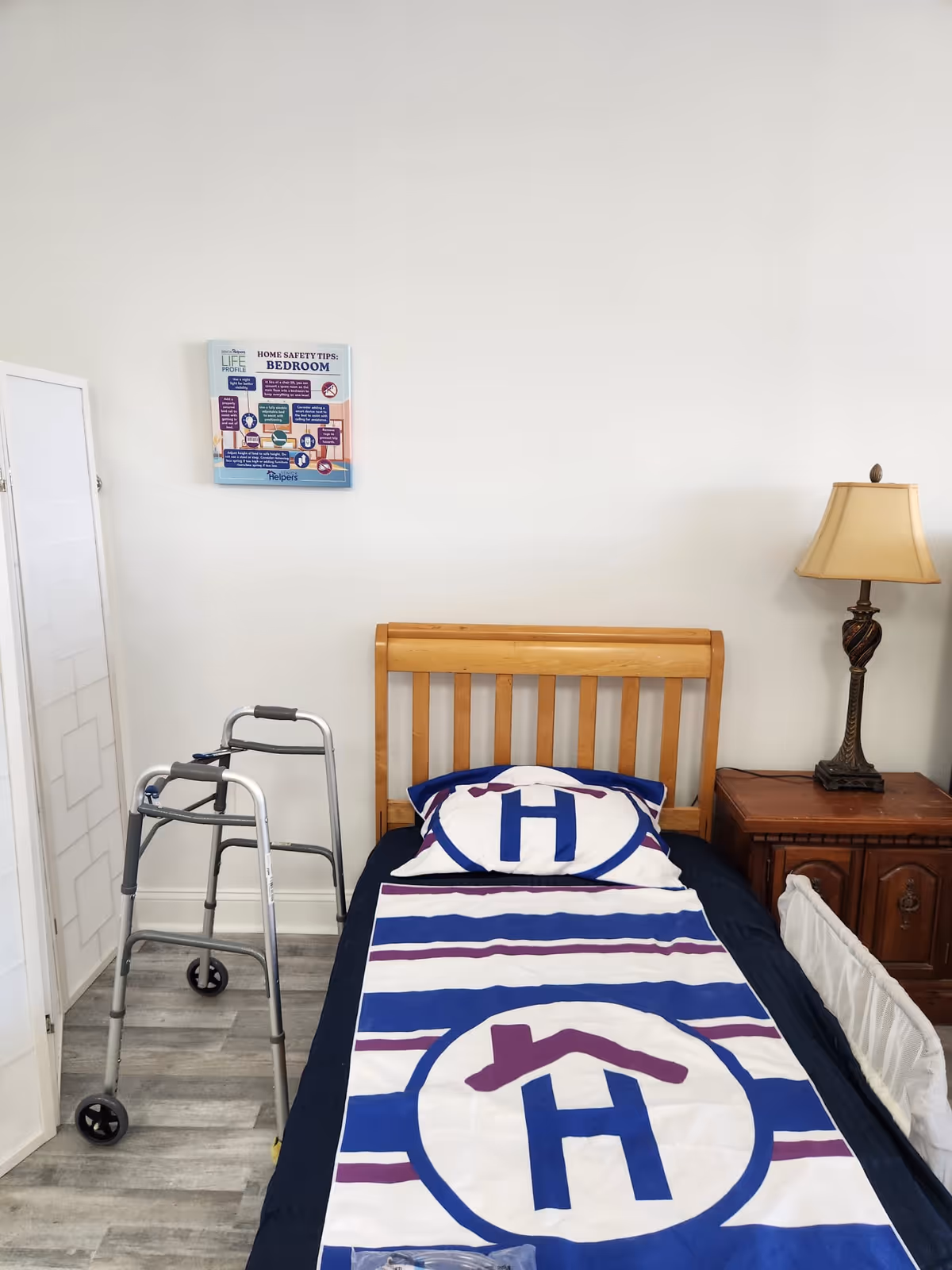 A small bedroom with a wooden bed, walker, nightstand, lamp, and safety poster.
