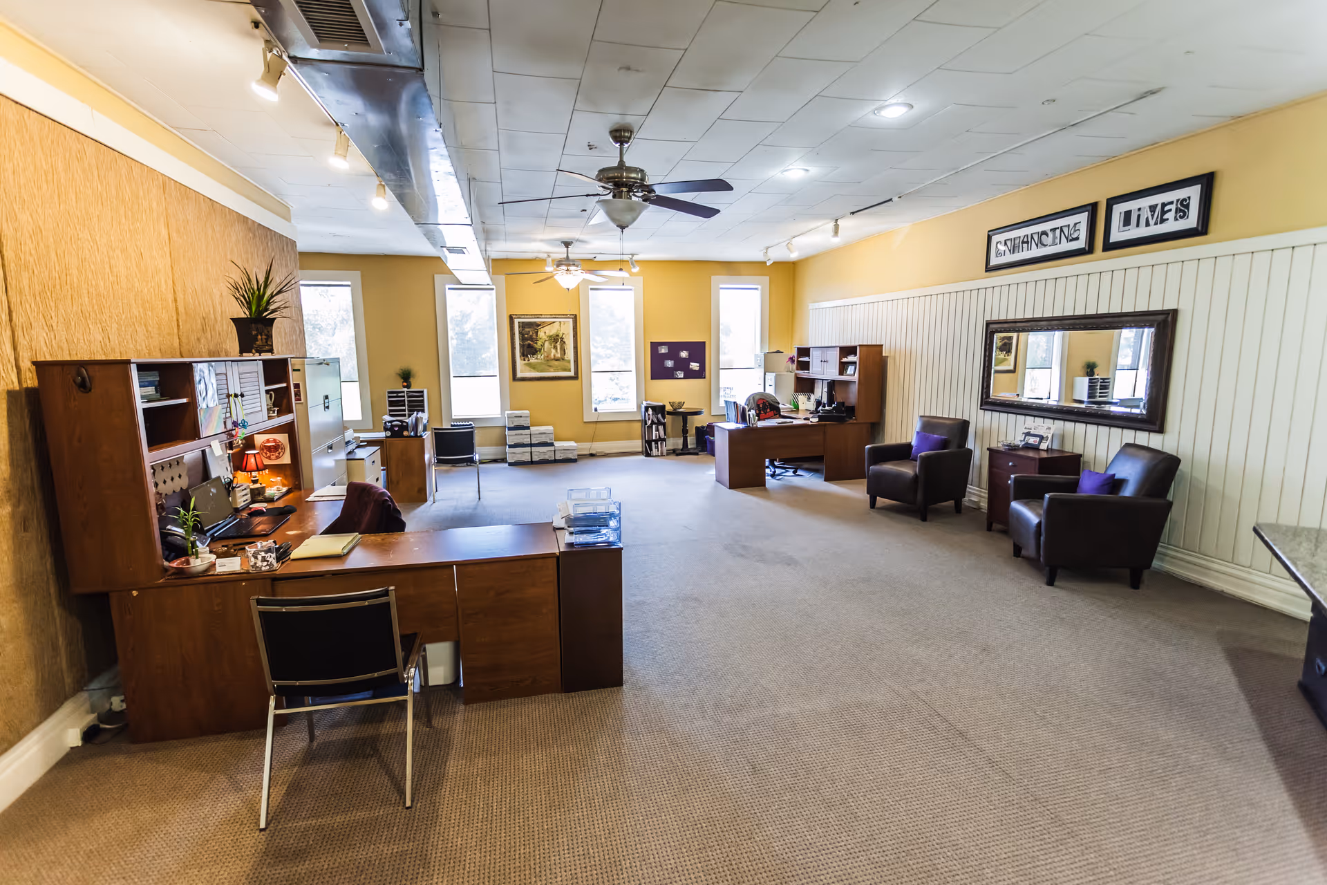 Open, well-lit senior living common area with desks, seating, and warm yellow walls.
