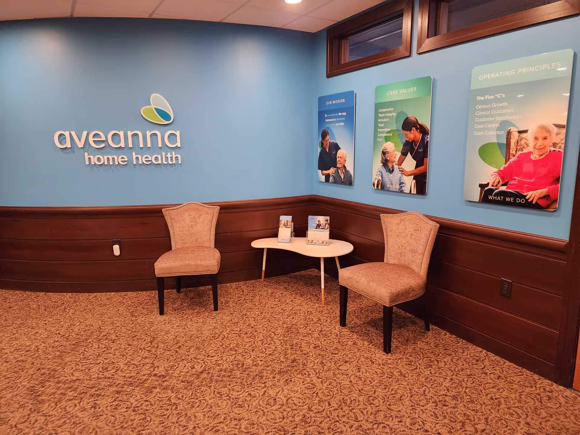 Lobby area featuring Aveanna Home Health logo on blue wall, two beige chairs, and brochures.