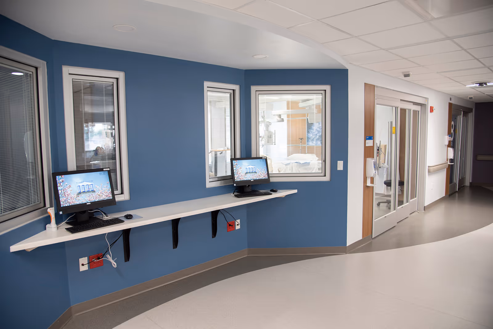 Blue-walled hospital corridor with a long white desk and two computer stations.