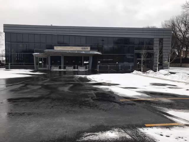 Modern glass-front facility exterior with a snow-covered parking lot and main entrance.