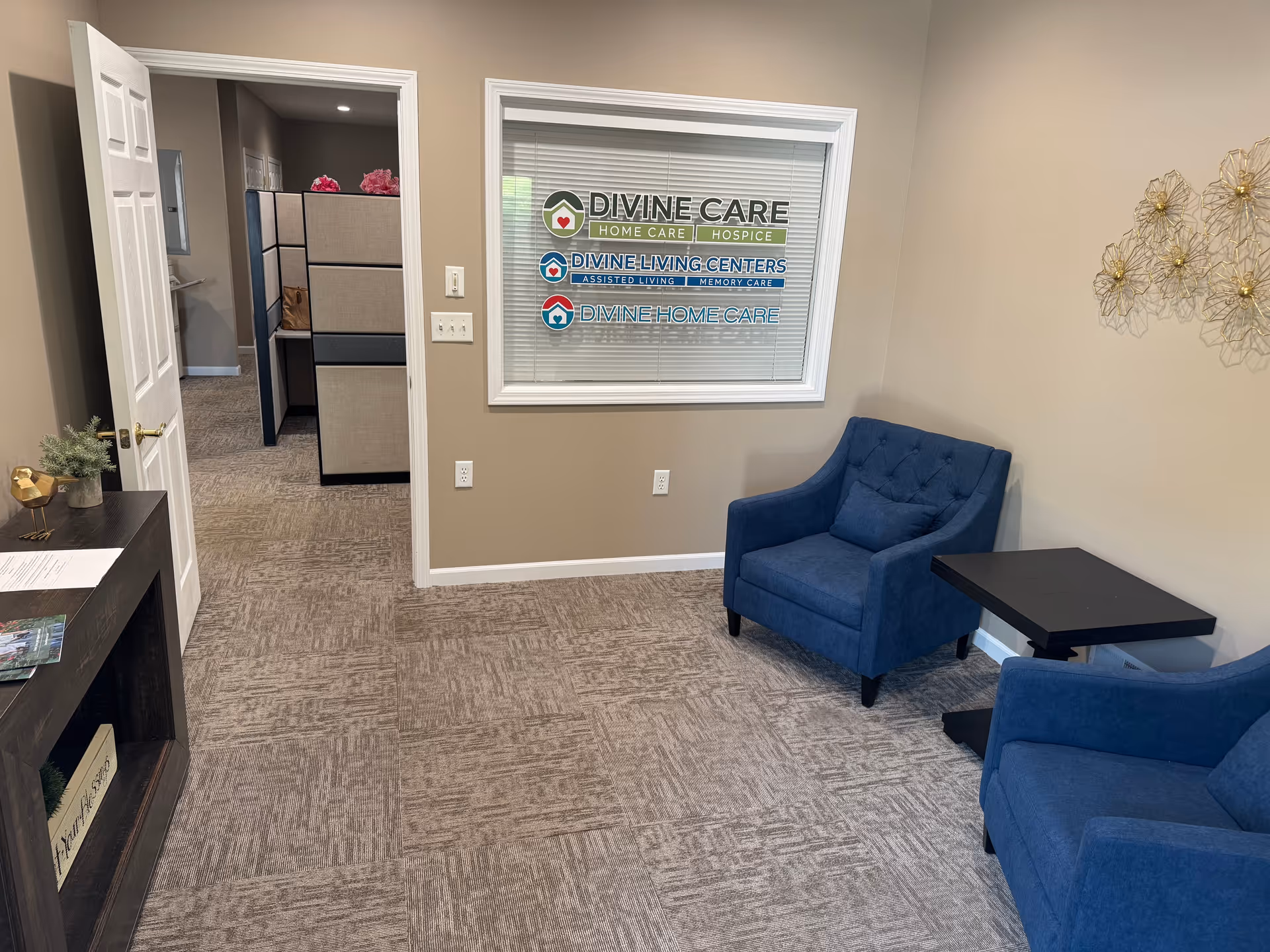 Reception area with blue chairs, a black table, and a window sign for Divine Care.