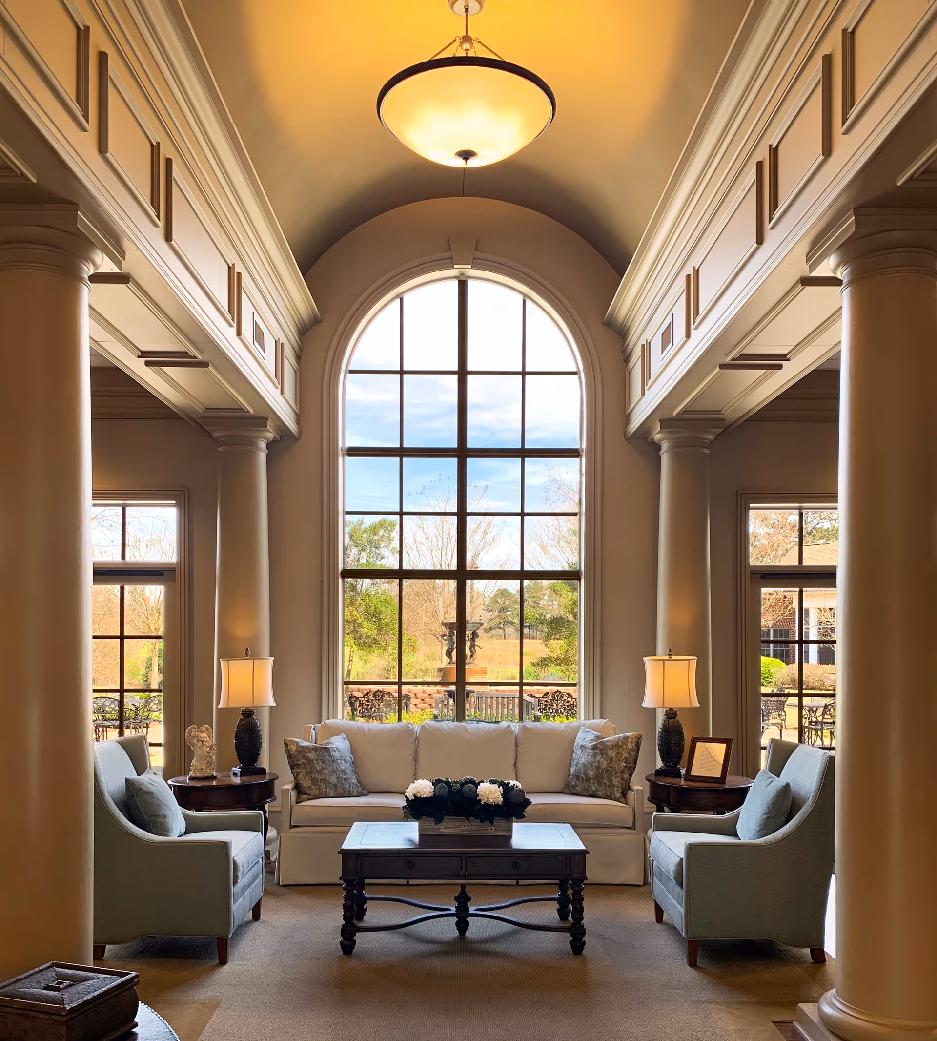 Elegant living room with a large arched window, sofa, chairs, and coffee table.