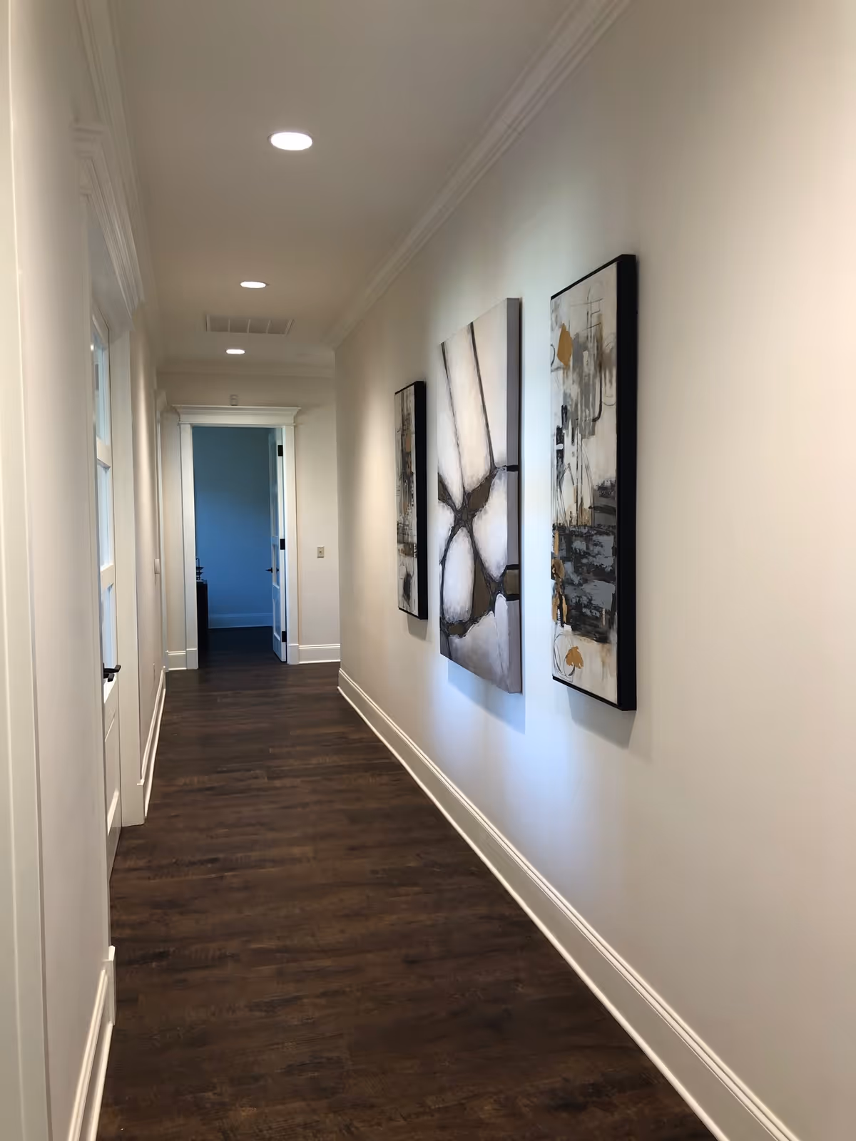 A clean, well-lit hallway with wall art and dark wood flooring.