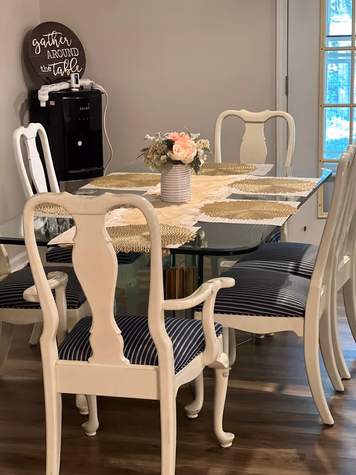 Glass dining table with six white chairs and a floral centerpiece.