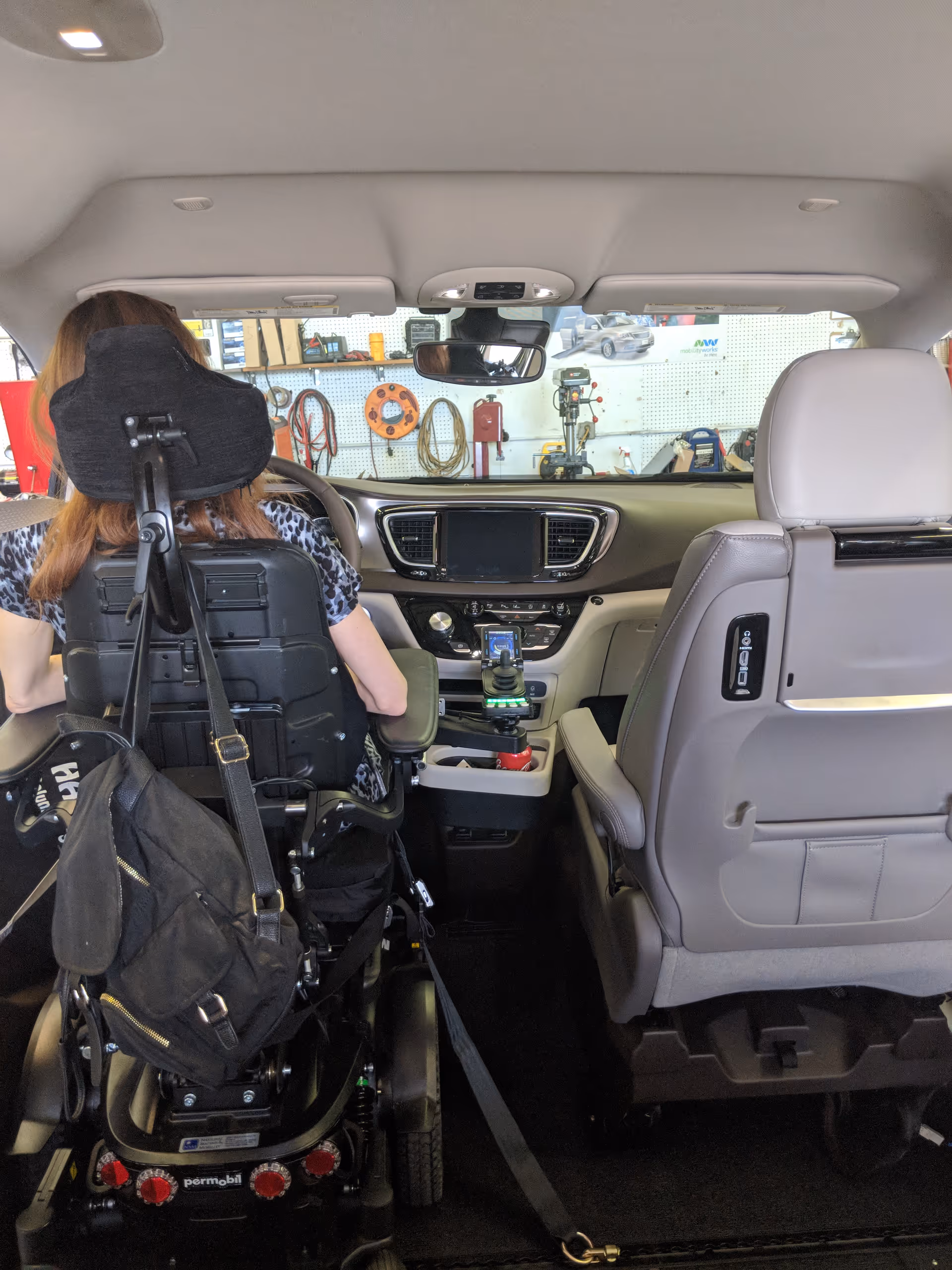 Interior of a vehicle showing a wheelchair user in the back, front dashboard, and equipment.