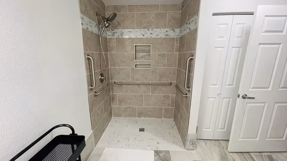 Accessible bathroom shower with grab bars, tiled walls, and a doorway on the right.