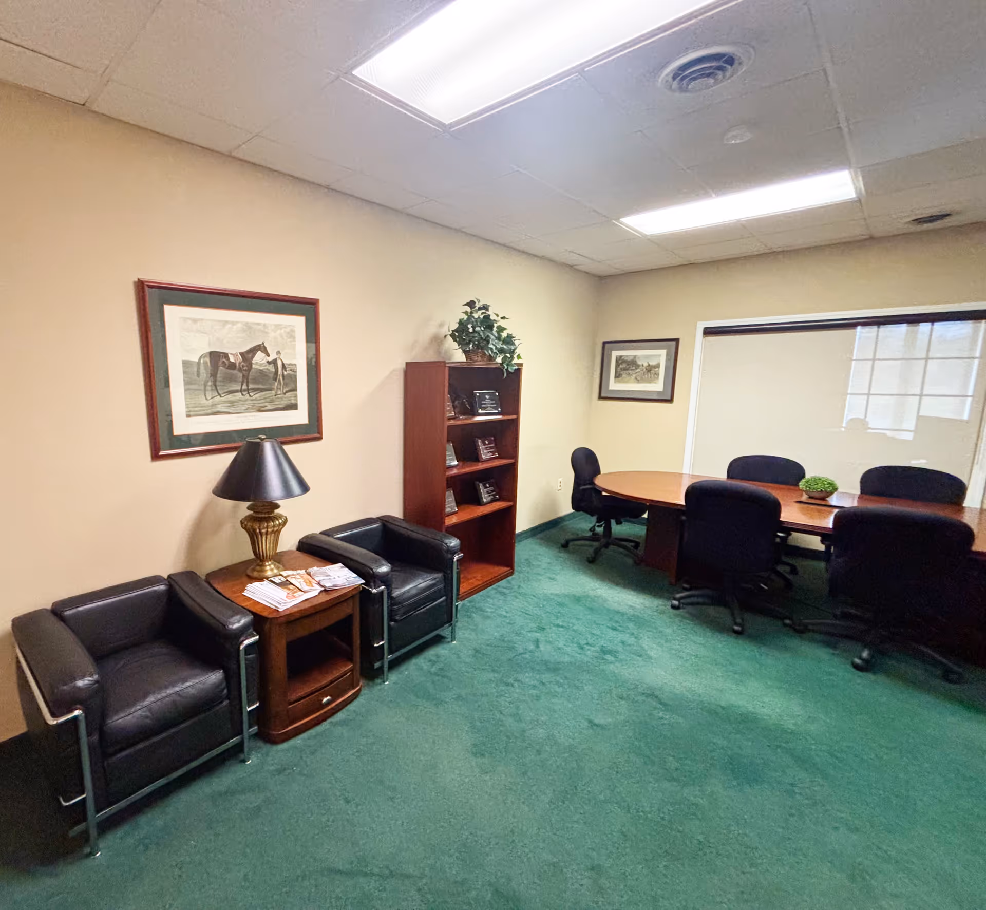 Interior waiting area with black leather seating, a round conference table, bookshelf, and plants.