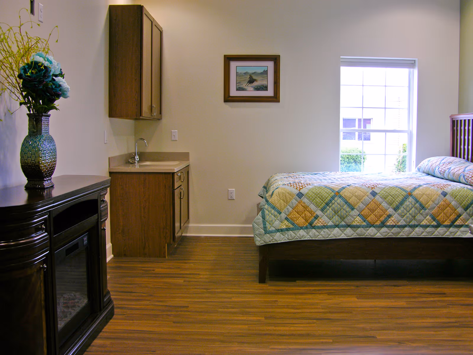 Senior living bedroom with bed, kitchenette area, and large window