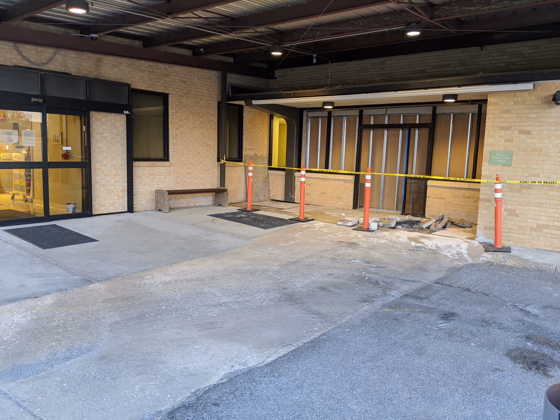 Exterior facility entrance with yellow caution tape, orange cones, and construction debris.