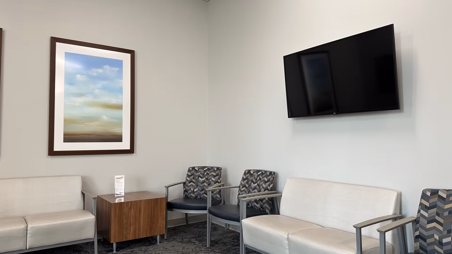 Neutral seating area in a senior living facility with a wall-mounted TV and framed artwork.