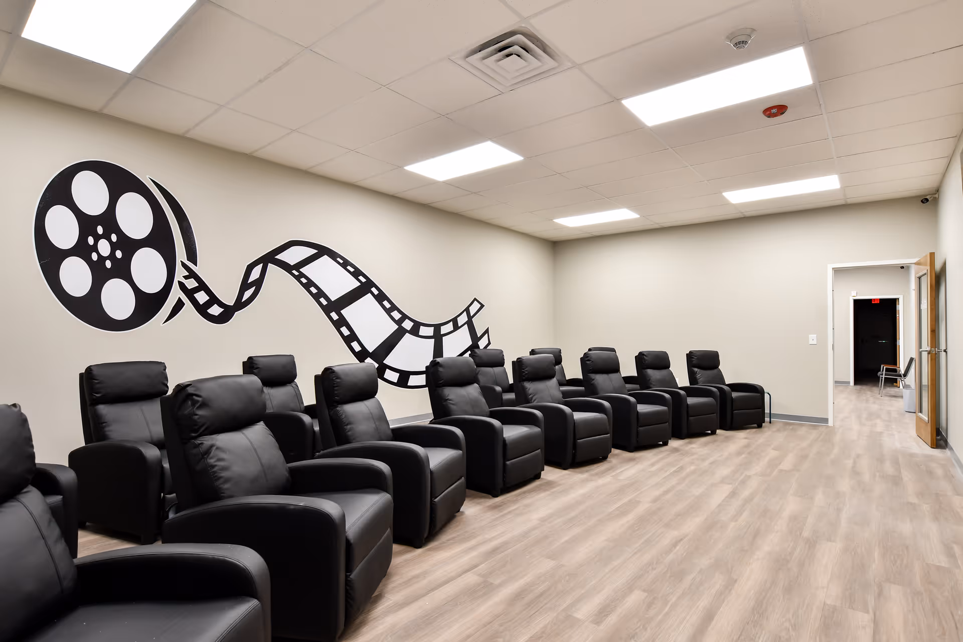 A spacious lounge with black recliner chairs arranged along a muraled wall.
