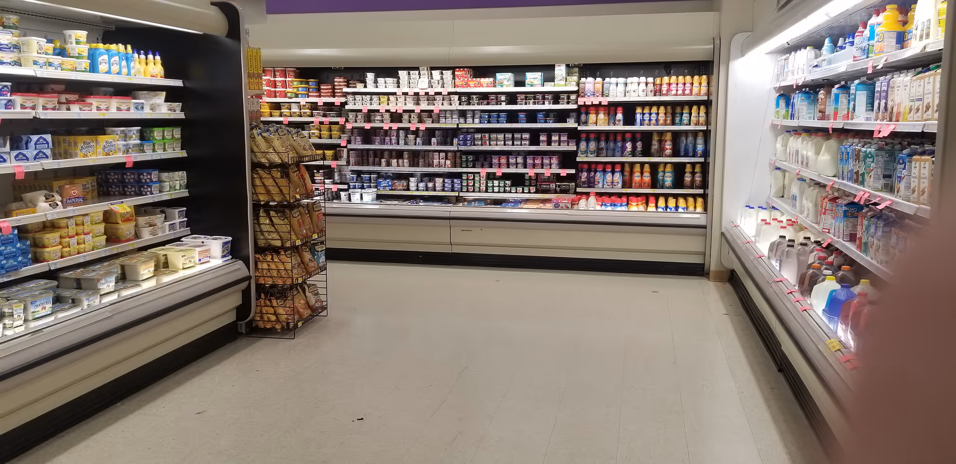 A narrow grocery-store aisle with refrigerated dairy shelves and beverages on both sides.