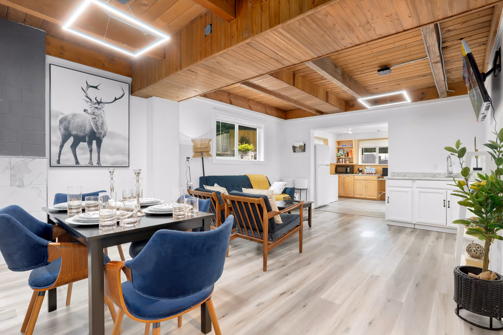 Open-concept living area showing dining table, blue chairs, sofa seating, and kitchen in background.