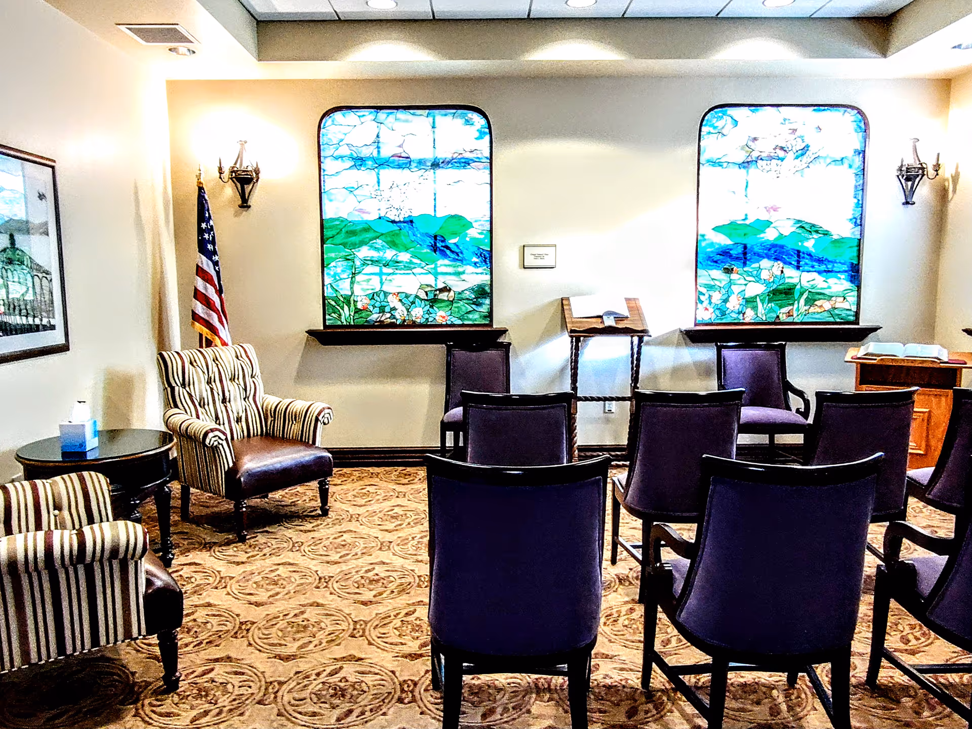 This indoor chapel has rows of chairs, a lectern, stained glass windows, and an American flag.