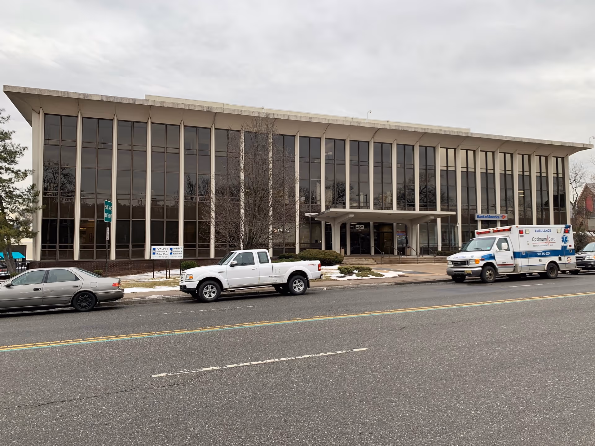 Glass-front building on a street with parked cars and an ambulance outside.