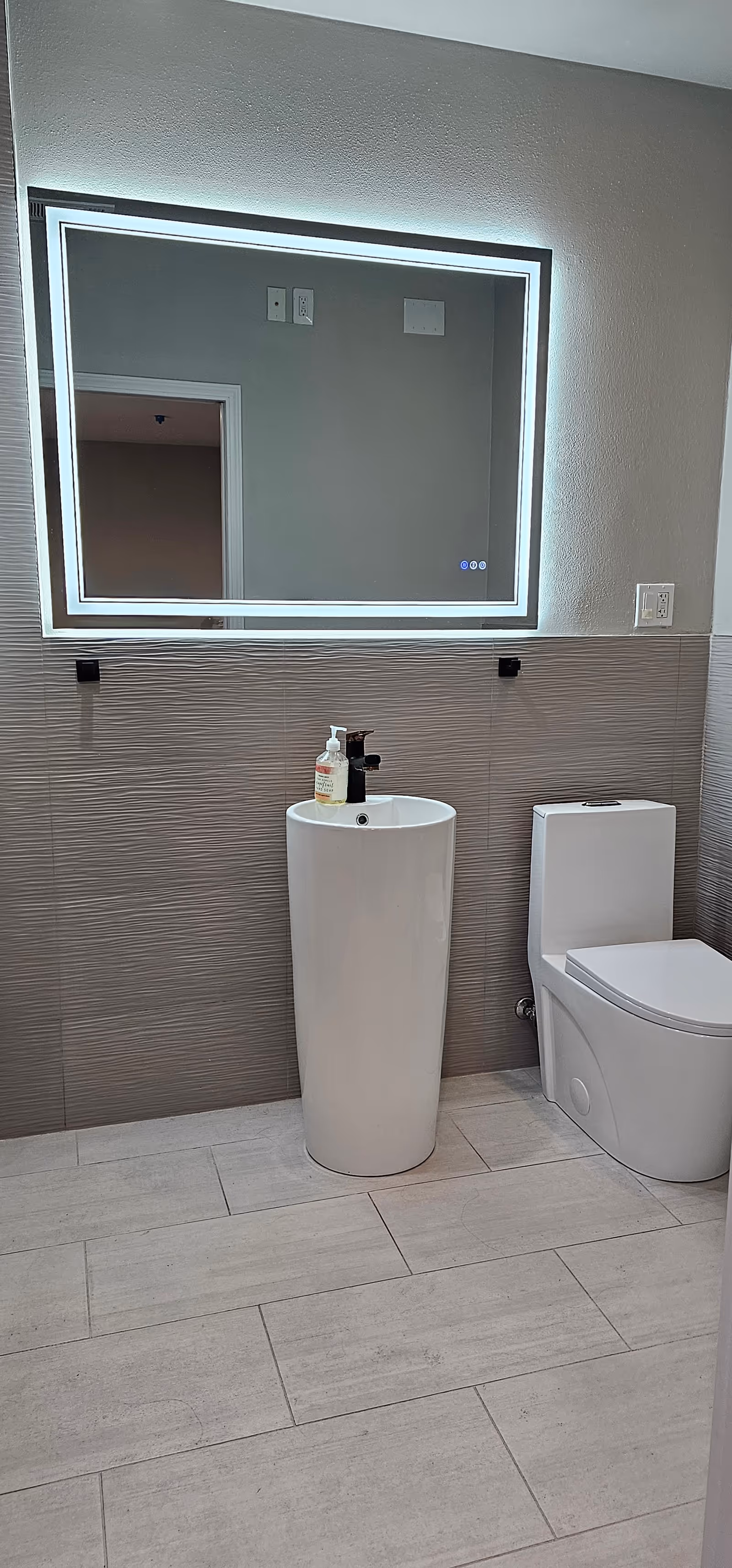 Modern bathroom with pedestal sink, toilet, and backlit framed mirror.