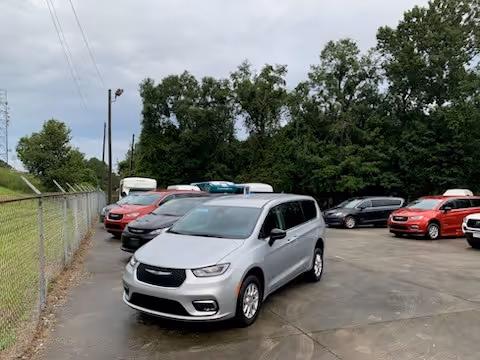 Several vans and cars parked in a spacious outdoor lot near a chain-link fence.