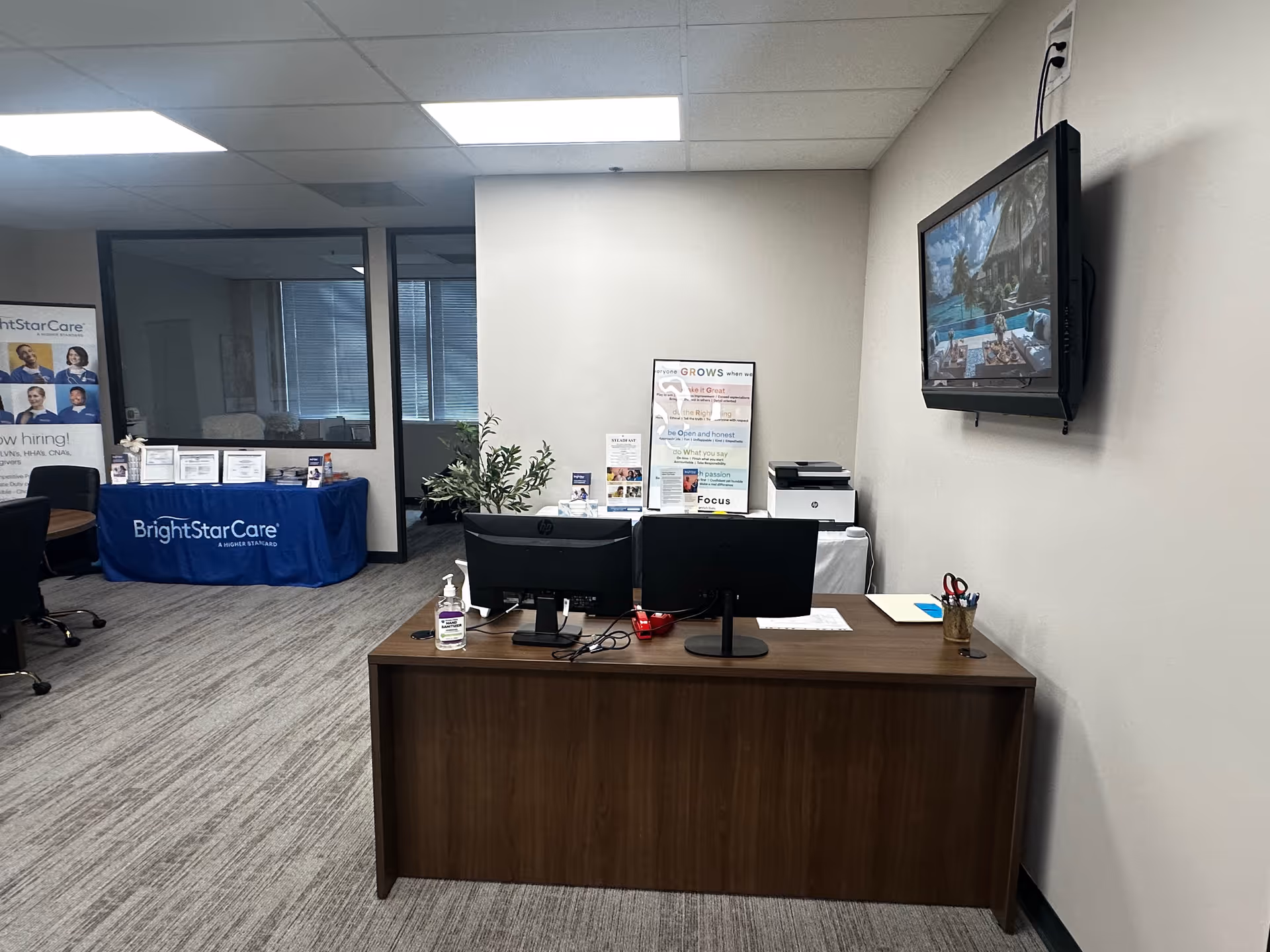 Reception desk with dual monitors, files, and a mounted TV in a BrightStar Care office.