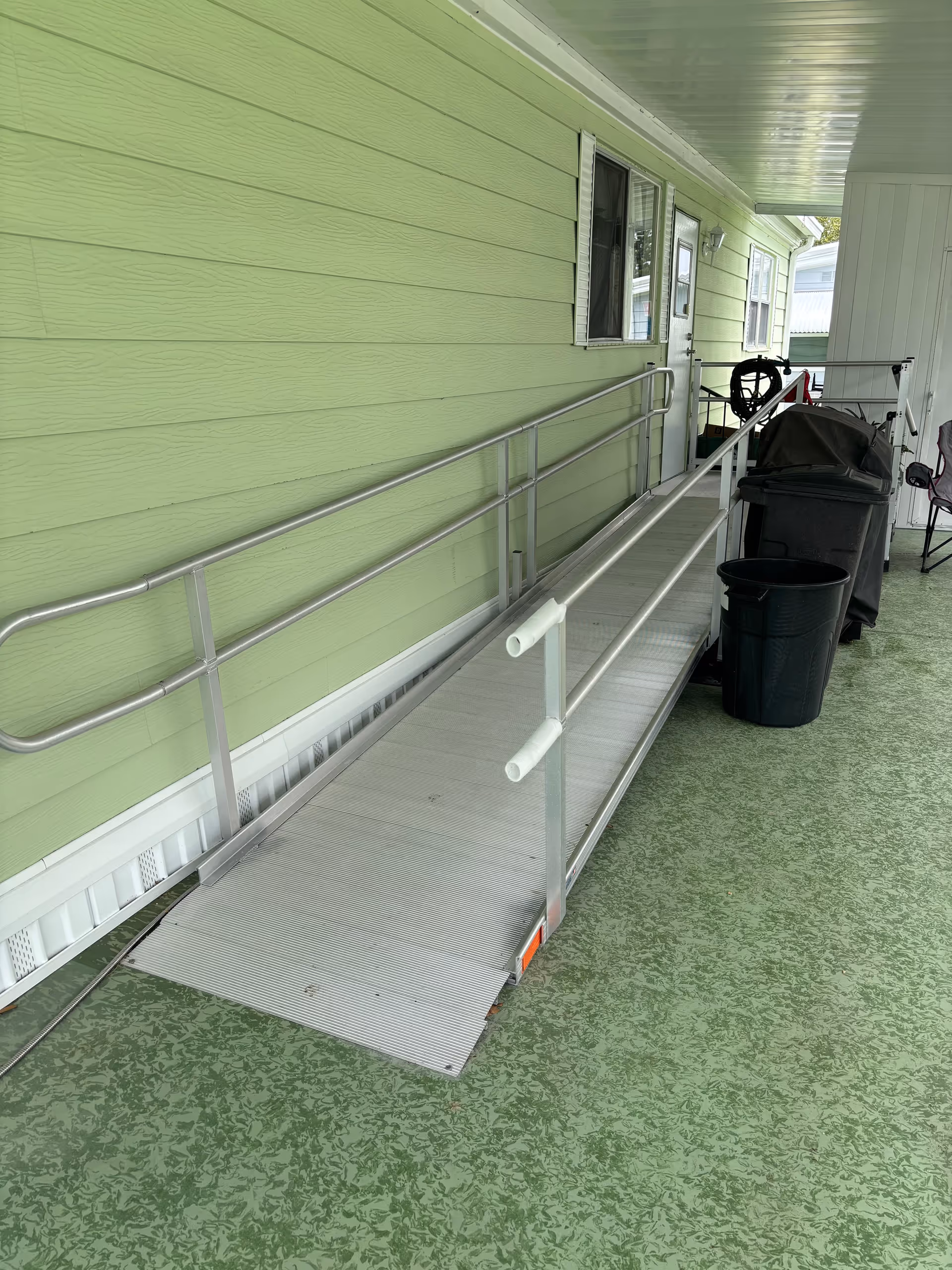 Green exterior walkway with a metal wheelchair ramp, railing, and a door.