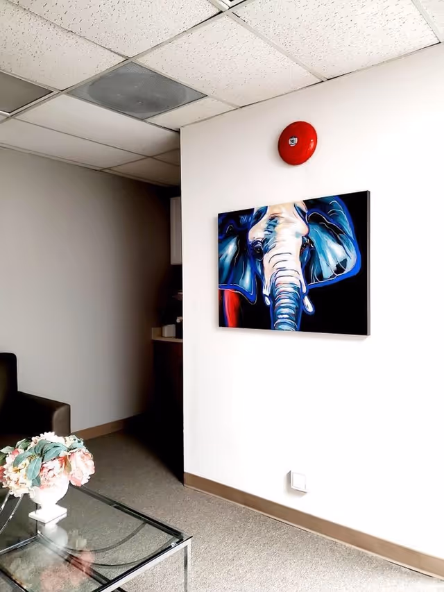 Modern lobby area with a glass coffee table, flower arrangement, and elephant painting.