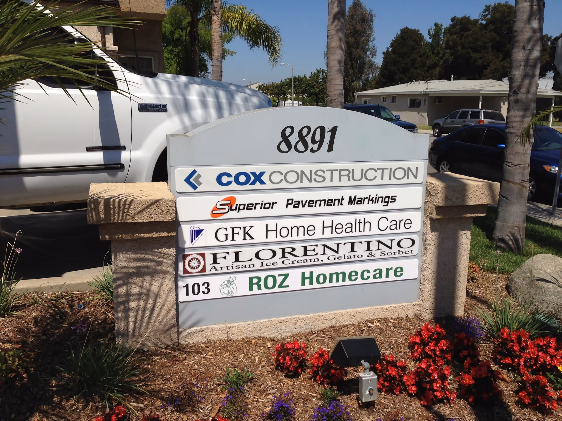 Outdoor sign displays Roz Homecare among other business names at a landscaped facility entrance.