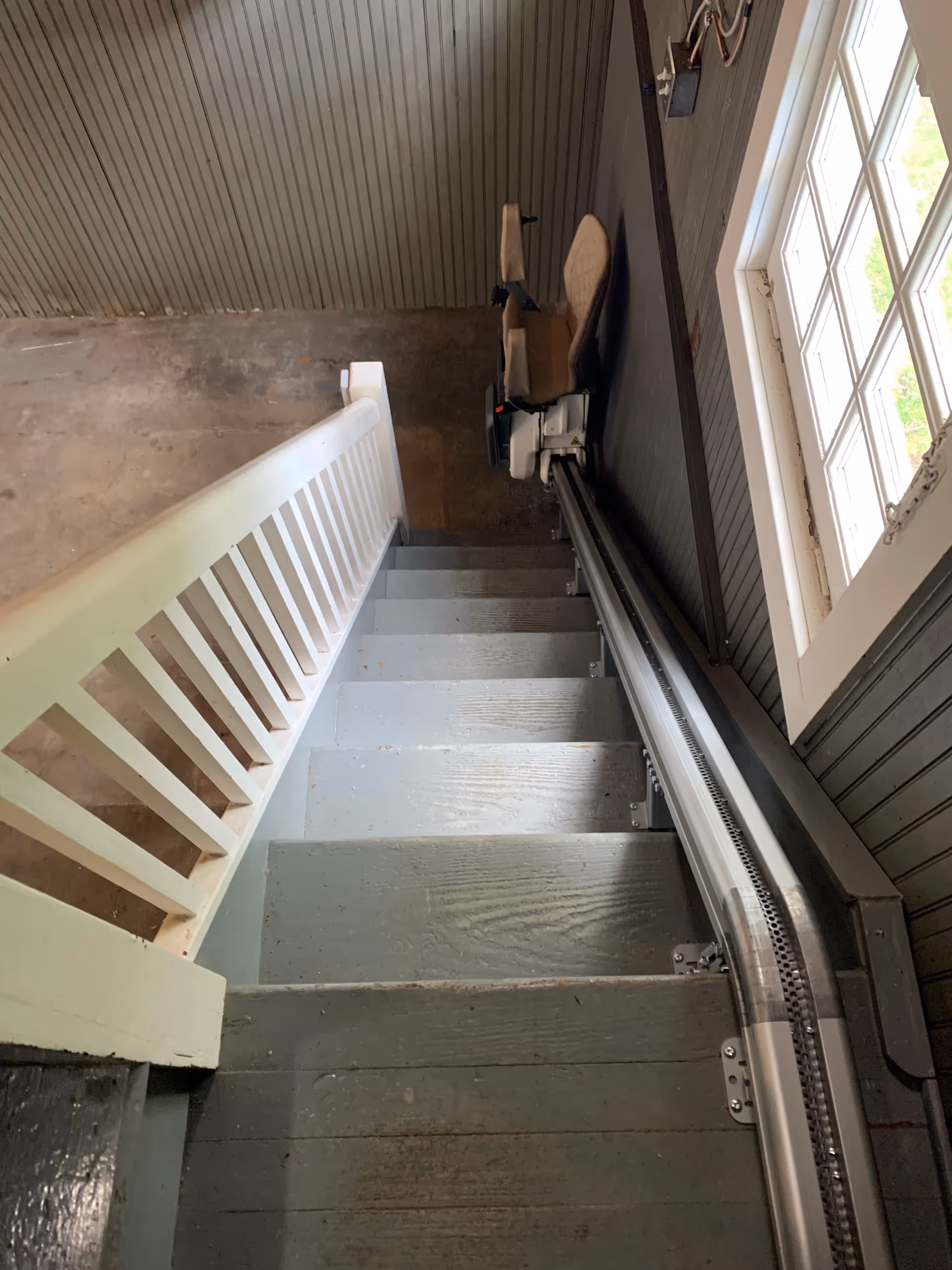 Interior stairwell with a chair on the landing and a stairlift rail along the wall.