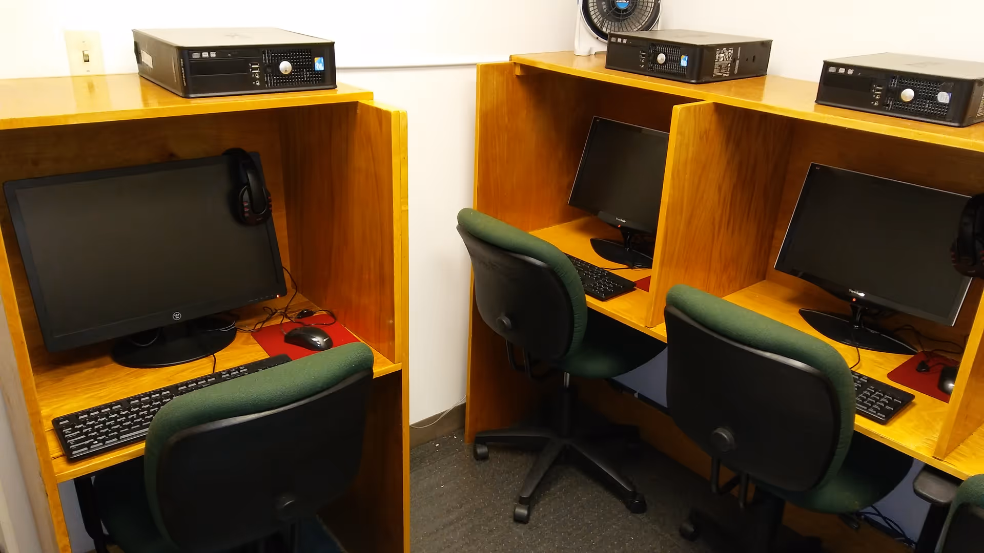Three computer cubicles with monitors and keyboards in a wood-furnished interior computer lab.
