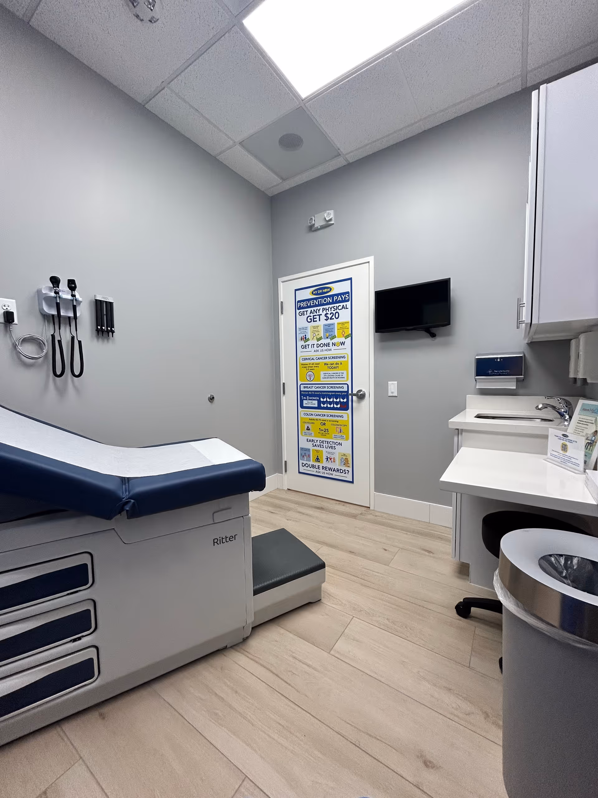 Interior medical examination room featuring an exam bed, wall-mounted tools, and a sink.